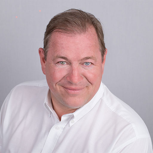 Porträt von Frank Chmielewski: lächelnder Mann im weißen Hemd vor grauem Hintergrund.