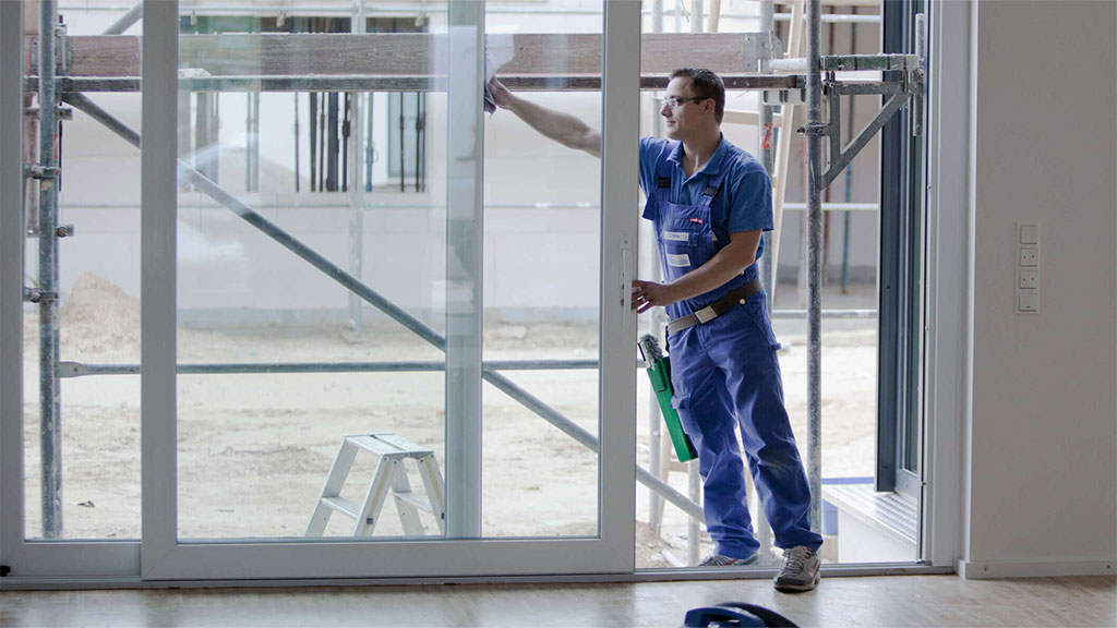Mitarbeiter bei der Glasreinigung an großer Tür in einem Neubau.