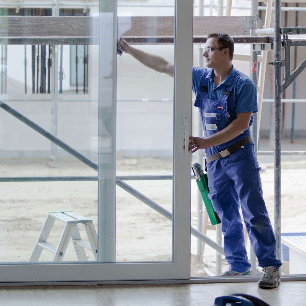 Mitarbeiter bei der Glasreinigung an großer Tür in einem Neubau.